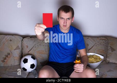 giovane in uniforme guardando il calcio in tv e mostrando la carta rossa Foto Stock