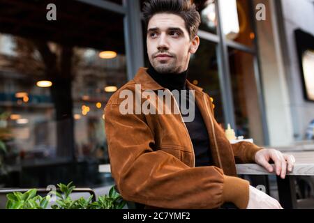 Giovane e attraente uomo informale che guarda via con attenzione nel cafe sulla strada Foto Stock