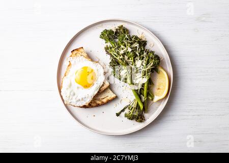 Broccolini arrosto, limone, uova fritte con tost sul piatto sul tavolo. Vista dall'alto su cibi sani. Foto Stock