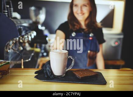 Barista che indossa guanti medici in lattice nero, rendendo rosa matcha latte con latte. Barista preparando una bevanda gustosa e una torta brownie Foto Stock