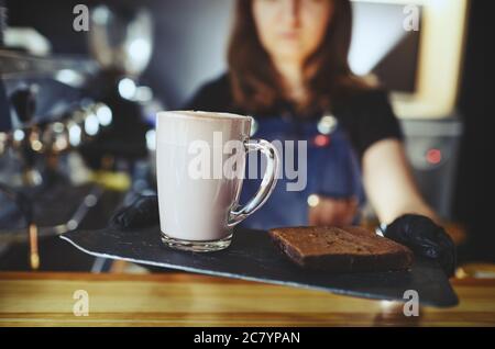 Barista che indossa guanti medici in lattice nero, rendendo rosa matcha latte con latte. Barista preparando una bevanda gustosa e una torta brownie Foto Stock