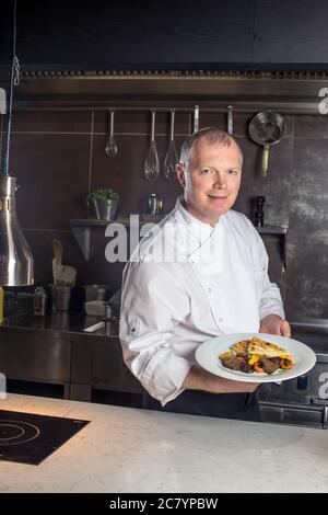 Ritratto di un maschio sorridente chef con il cibo cotto in piedi in cucina Foto Stock