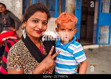 Agra / India - 13 febbraio 2020: Ritratto di giovane madre indù indiana che tiene il suo figlio mentre sorride alla macchina fotografica e facendo segno di vittoria con le dita Foto Stock