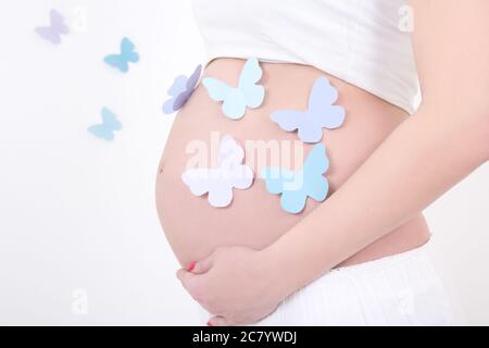 ventre di donna incinta con farfalle colorate su sfondo bianco Foto Stock