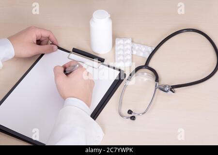 primo piano di mani di medico maschile, stetoscopio e pillole sul tavolo Foto Stock