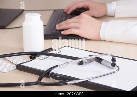 primo piano di stetoscopio, cartella e mani del medico che digitano sulla tastiera Foto Stock