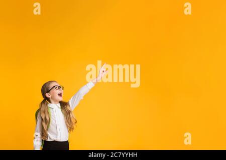 Scuola elementare ragazza che punta dito che posa sopra sfondo giallo Studio Foto Stock