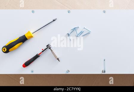 Mobili bianchi in procce di raccolta. Cacciavite per utensili manuali sul ripiano dell'armadio. Movimento, miglioramento della casa, riparazione e ristrutturazione di mobili. Vista dall'alto Foto Stock