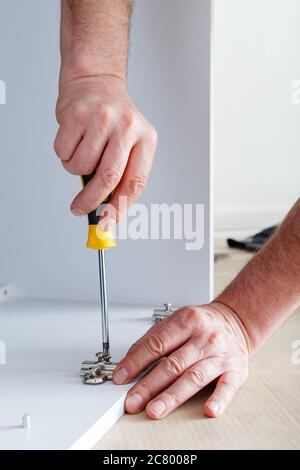 La falegname raccoglie i mobili utilizzando un cacciavite a mano. Montaggio di mobili con cacciavite. Movimento, miglioramento della casa, riparazione di mobili e. Foto Stock
