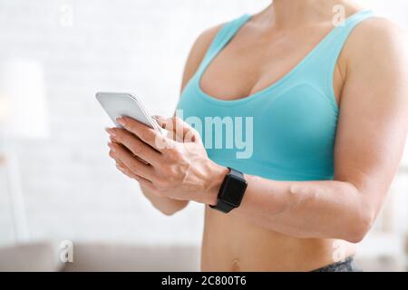 Palestra. Donna con orologio intelligente e telefono in mano in interni leggeri Foto Stock