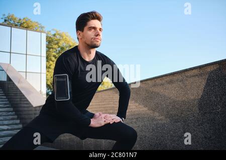 Giovane bell'uomo sportivo che si stretola con cura durante l'allenamento mattutino nel parco Foto Stock