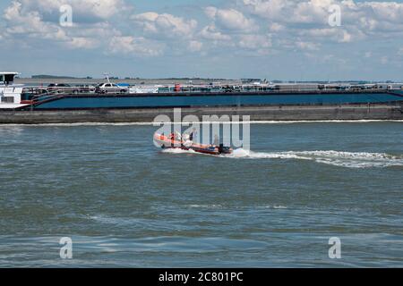 Terneuzen, Paesi Bassi, 12 luglio 2020, un motoscafo in gomma arancione con sei persone sta navigando accanto a una grande nave Foto Stock