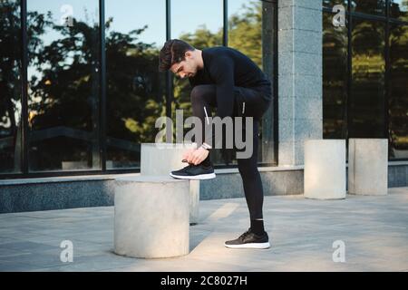 Vista laterale delle scarpe da ginnastica per uomo giovane e sicuro che legano le scarpe da ginnastica in città Foto Stock