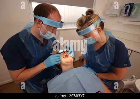 Il dentista Dr. Allan Clarke e l'infermiera dentale Lynsey Galaway (destra) indossando PPE con il collega dentista Dr. Danielle Magee per mostrare nuove procedure di allontanamento sociale in una pratica a Belfast. Foto Stock