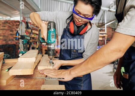 Carpernter guardando giovane donna che fora per la prima volta in tavola di legno Foto Stock