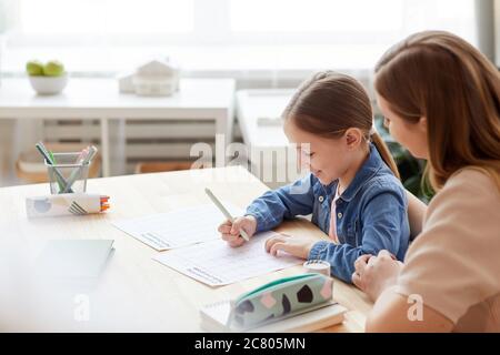 Ritratto di sorridente bambina facendo test di matematica per la scuola online mentre studiando a casa con la madre premurosa o tutor aiutandola, copia spazio Foto Stock