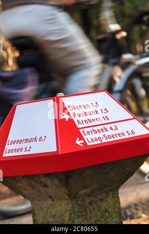 Un cartello rosso per la pista ciclabile nel parco nazionale olandese di Veluwe con un ciclista sul retro Foto Stock