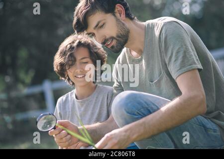 Ragazzo dai capelli scuri e suo padre che guarda la pianta attraverso la lente d'ingrandimento Foto Stock