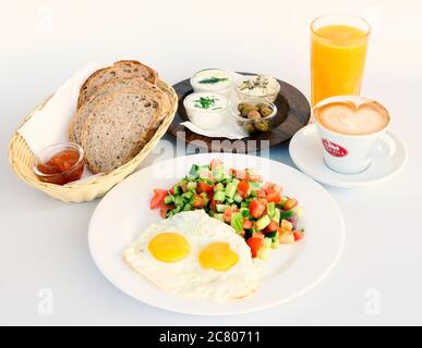 Colazione israeliana con due uova fritte, insalata, pane, burro, formaggi, succo d'arancia e caffè Foto Stock