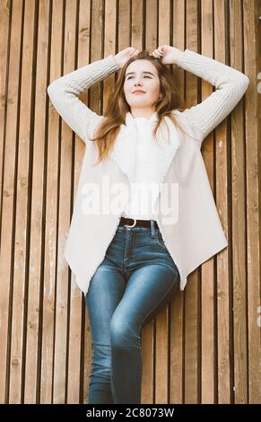 Ritratto di bella ragazza giovane con lunghi capelli marroni sdraiati e rilassante su sfondo di legno di tavole, inverno o autunno all'aperto foto con Foto Stock