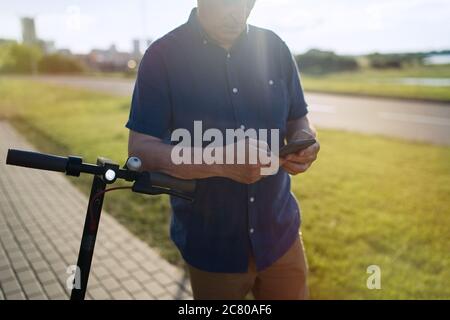 Uomo anziano che usa lo smartphone dopo aver cavalcato con un calciatore elettrico Foto Stock