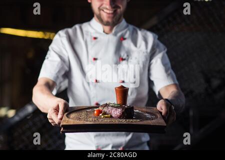 Ritratto di un maschio sorridente chef con il cibo cotto in piedi in cucina Foto Stock