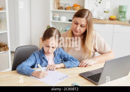 Ritratto di donna adulta che aiuta la ragazza a fare i compiti o studiare a casa mentre si siede alla scrivania in interni accoglienti, spazio di copia Foto Stock