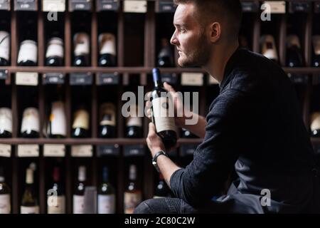 Sommelier maschile concentrato in suite guardando il vino rosso in bottiglia Foto Stock