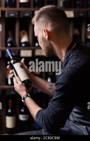 Sommelier maschile concentrato in suite guardando il vino rosso in bottiglia Foto Stock