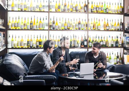 Ritratto giovane sommelier seduto in cantina di famiglia con due enologo e degustazione di un bicchiere di vino rosso. Piccole imprese. Foto Stock