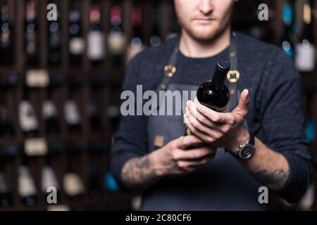 Sommelier maschile concentrato in suite guardando il vino rosso in bottiglia Foto Stock