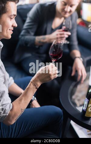 Focalizzato giovane maschio sommelier in suite guardando il vino rosso in vetro su sfondo bianco Foto Stock