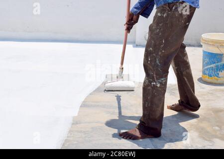 Rivestimento del tetto vernice bianca su un tetto di cemento un uomo pittura sulla parte superiore del tetto per ridurre il calore sulla casa verniciando vernice bianca del rivestimento del tetto che riflette il sole Foto Stock