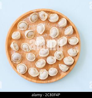 Pelmeni grezzi o gnocchi russi su una piastra di legno. Foto Stock