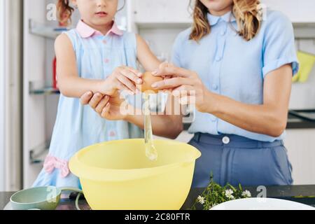 Madre insegnando alla figlia come rompere le uova nella ciotola quando fa l'impasto del biscotto Foto Stock
