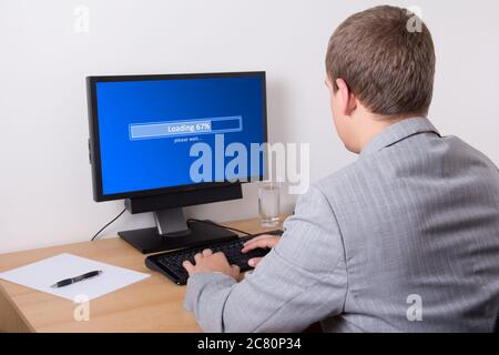 giovane uomo d'affari che scarica qualcosa da internet usando il personal computer in ufficio Foto Stock