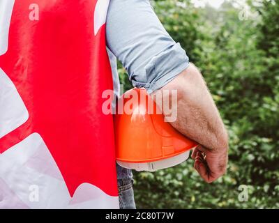 Bell'uomo con gli attrezzi, che tiene una bandiera canadese Foto Stock