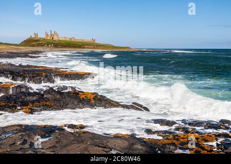 Onde che si infrangono sulle rocce nere del castello di Dunstanburgh, Northumberland, Inghilterra Foto Stock