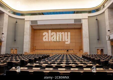 Interni, edificio delle Nazioni Unite, Ginevra. Sala riunioni dal retro alla parte anteriore con posti a sedere in primo piano e palco principale con il logo ONU sopra. Foto Stock