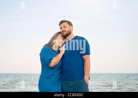 Uomo che abbuggia donna che sta in piedi spiaggia di mare. Relazione romantica sulla vacanza estiva ritratto due persone caucasiche Foto Stock