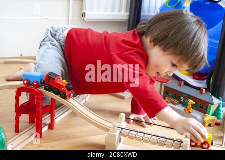 Bambino caucasico, 3-4 anni, all'interno. Il livello del pavimento vista del giovane ragazzo giocando con Thomas Tank Engine train set. Spingendo il treno lungo la via. Foto Stock