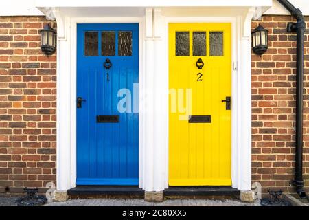 Casa esterna, due porte anteriori in legno e vetro. Telaio comune con una porta blu e una gialla, numerate 1 e 2. Entrambi identici all'altro. Foto Stock