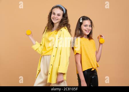 Due bambini giocosi giovani in camicie gialle, sorelle o ragazze biraciali pre teen con capelli ricci marroni che giocano o si esercitano, sollevando i manubri Foto Stock