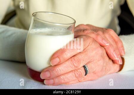 Mani che reggono un bicchiere di latte cremoso con un pizzico di fruttato su una superficie morbida in un ambiente sereno Foto Stock