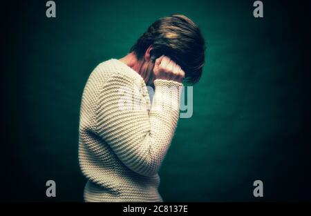 Donna dall'espressione angosciata che ricopre il viso in una stanza poco illuminata durante un momento emotivo Foto Stock