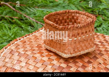 Tessuti a mano mat e cestello realizzato dal duttile di corteccia interna di un Western Red Cedar tree, poggiante su Western Red Cedar branchlets. Foto Stock