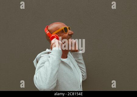 l'uomo anziano ascolta la musica su sfondi marroni con cuffie e occhiali da sole - ritratto dell'uomo adulto su sfondo marrone Foto Stock