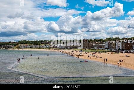 North Berwick, East Lothian, Scozia, Regno Unito, 20 luglio 2020. UK Weather: Divertimento estivo nella cittadina di mare con il caldo sole ma molto ventilato tempo. Vista sulla piscina e sul lungomare con la marea che si trova sulla East Beach di Milsey Bay Foto Stock