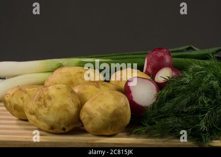 Patate giovani, ravanello, cipolle verdi, aneto su tavola di legno, fondo nero Foto Stock