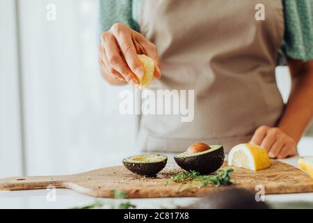 Le mani femminili stringono il limone sull'avocado mentre preparano il pasto sano Foto Stock